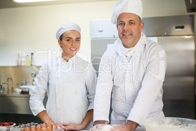 Smiling head chef showing trainee how to prepare dough