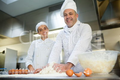 Happy head chef showing smiling trainee how to prepare dough