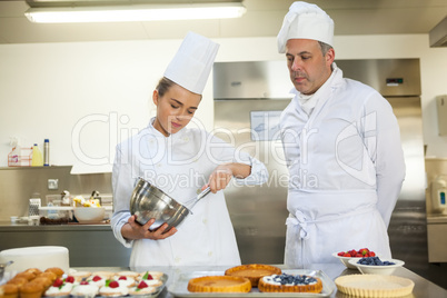 Serious chef whisking while being watched by head chef