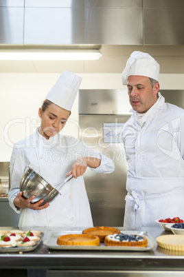 Frowning chef whisking while being watched by head chef