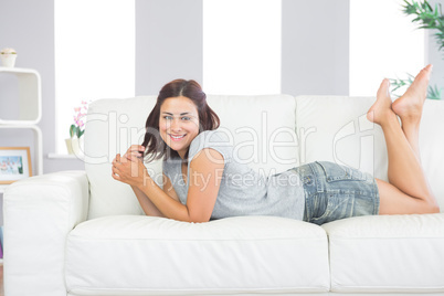 Portrait of pretty brunette woman lying on her couch in the livi