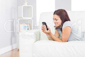 Content casual woman working with her smartphone while lying on