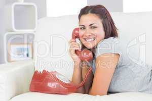 Amused young woman using a red dial phone