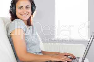 Cheerful casual woman listening to music and using her notebook
