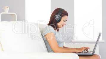 Cute casual woman witting on couch using her notebook and listen