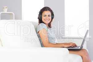 Cheerful young woman using her notebook and listening to music