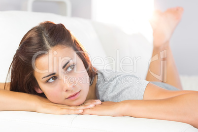 Melancholic young woman lying on her white couch