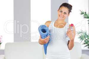 Young woman posing holding an exercise mat and a bottle in her l