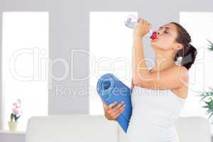 Attractive woman drinking out of a bottle while holding an exerc
