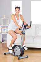 Cheerful young woman training on an exercise bike in her living