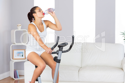 Lovely slender woman drinking while training on an exercise bike