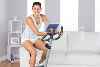 Cheerful sporty woman training on an exercise bike while holding