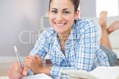 Portrait of beautiful young student doing assignments lying on t