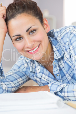 Pretty brunette student smiling at camera while lying on the flo