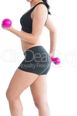 Mid section of slim young woman training her arms with pink dumb