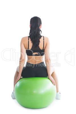 Rear view of slender ponytailed woman sitting on an exercise bal