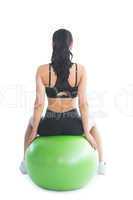Rear view of slender ponytailed woman sitting on an exercise bal