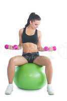 Sporty slim woman training her arms with dumbbells sitting on an