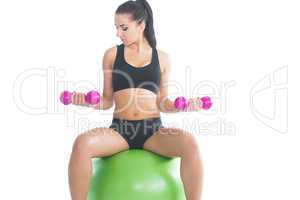 Concentrating sporty woman using dumbbells sitting on an exercis