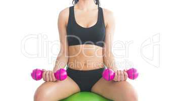 Mid section of slender fit woman training with dumbbells sitting