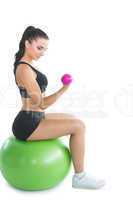 Attractive young woman sitting on an exercise ball using pink du