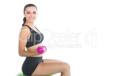 Beautiful slim woman using pink dumbbells sitting on an exercise