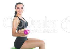 Beautiful slim woman using pink dumbbells sitting on an exercise