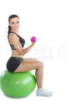 Cheerful active woman sitting on an exercise ball using pink dum