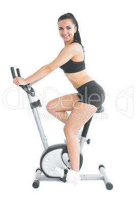 Slender fit woman training on an exercise bike smiling at camera