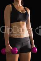 Mid section of fit slender woman holding pink dumbbells