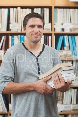 Mature student posing in library holding a pile of books