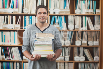 Attractive librarian holding a pile of books standing in library