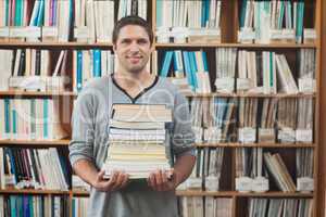 Attractive librarian holding a pile of books standing in library