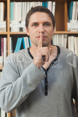 Male librarian making a sign to be quiet in library