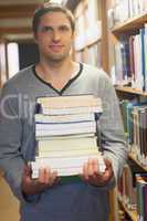 Handsome brunette librarian posing in library holding a pile of