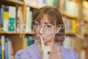 Mature female librarian giving a sign to be quiet standing in li