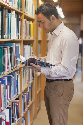 Handsome man reading concentrated a book standing in library