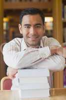 Attractive man posing in library leaning on a pile of books