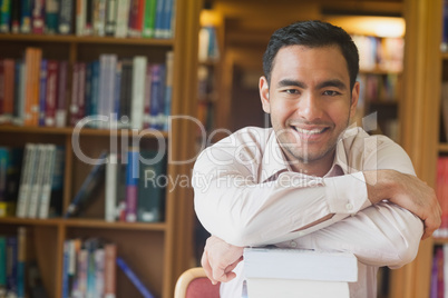 Cheerful attractive man posing leaning on a stack of books in li