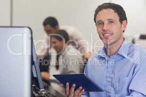 Male student holding a tablet sitting in front of computer