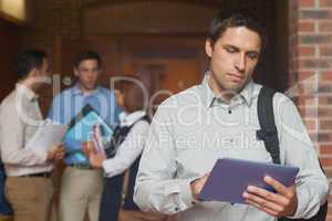 Concentrated male mature student holding his tablet standing in