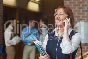 Amused mature student phoning standing in corridor
