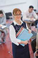 Pretty female teacher posing in her classroom holding some files