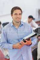 Cute male teacher holding some files while posing in his classro