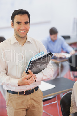 Handsome black haired teacher posing in his classroom holding so