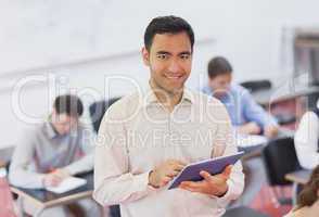 Cute teacher holding his tablet while posing in his classroom