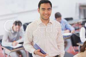 Cheerful male teacher posing in his classroom holding a tablet