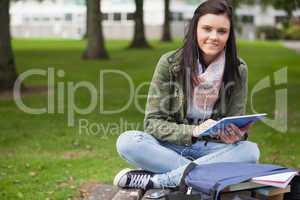 Happy brunette student using tablet sitting on bench