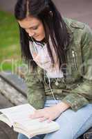 Content brunette student sitting on bench reading