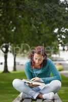 Focused casual student sitting on bench reading
